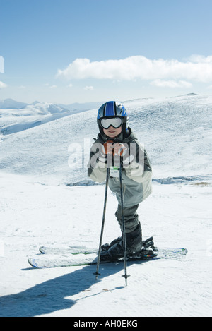 Young skier leaning on ski sticks, smiling at camera, full length portrait Stock Photo