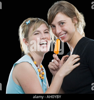 Portrait of a young woman holding an ice-cream with her friend laughing Stock Photo