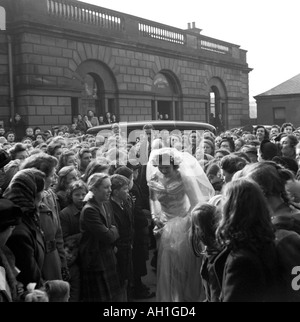 OLD VINTAGE FAMILY SNAPSHOT PHOTOGRAPH OF BRIDE WEARING WHITE SATIN BRIDAL GOWN WALKING THROUGH LARGE CROWD TO WEDDING CEREMONY Stock Photo