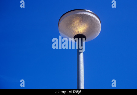 Street lamp with frosted glass or plastic cover and aluminium pole glowing against a clear deep blue sky Stock Photo