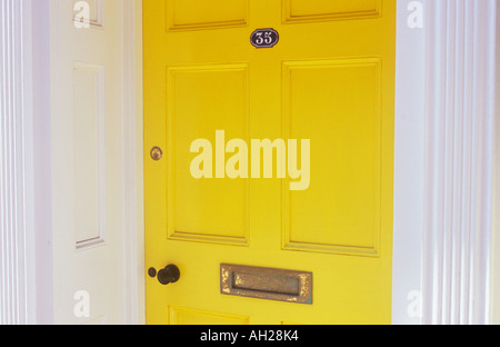 Detail of yellow painted front door with blue enamel house number plate letterbox and stylish mouldings in warm reflected light Stock Photo