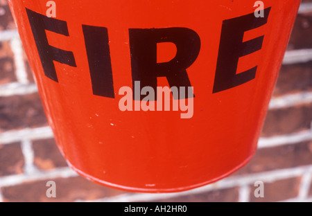 Close up of a bright red aluminium bucket with bold black letters stating FIRE suspended on a dark ochre brick wall Stock Photo