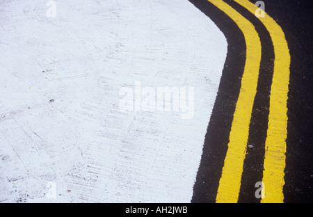 Detail of freshly painted double yellow lines curving around a white painted no access area on new tarmac Stock Photo