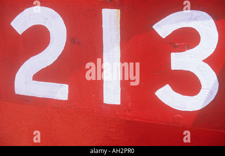 Close up of white numbers 213 painted on the red surface of a boat with ...