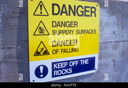 Close up of sunlit sign on jetty or promenade stating Danger Slippery surfaces Danger of falling Keep off the rocks Stock Photo