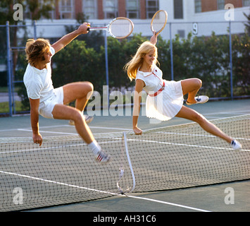 couple leaping net on tennis court Stock Photo