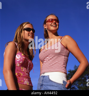 Beautiful trendy smiling teens teenagers friends girls wearing sunglasses and summer tops smiling in blue sky sunshine in Wales UK   KATHY DEWITT Stock Photo