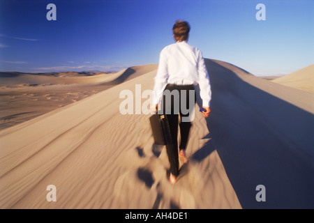 Businessman with briefcase walking on sand dune in Nevada Stock Photo