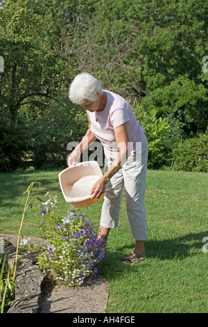 Woman using waste washing up water to water plants in garden Cotswolds UK Stock Photo