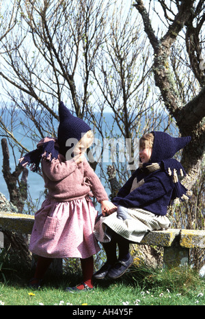 Two little girls wearing winter clothes laughing and sitting on a stone wall Stock Photo