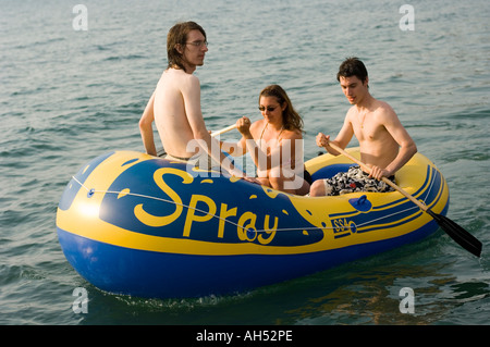 Three young people friends having fun in an inflatable dinghy on the sea on a summer afternoon Wales UK Stock Photo