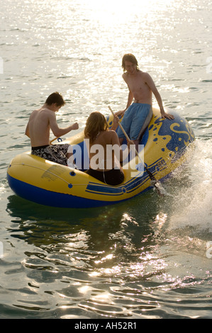 Three young people friends having fun in an inflatable dinghy on the sea on a summer afternoon Wales UK Stock Photo