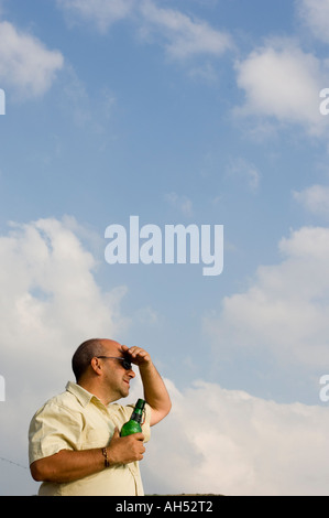 Middle aged man with bottle of beer in hand, shielding his eyes from the sun Stock Photo