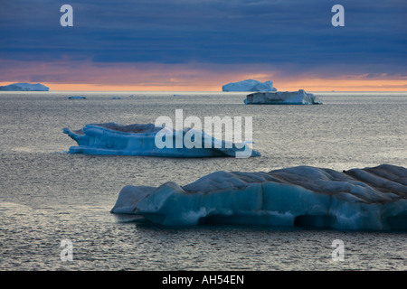 Icebergs on a calm sea against dramatic leaden grey blue sunset sky in Davis Strait near Ilulissat off west coast of Greenland Stock Photo