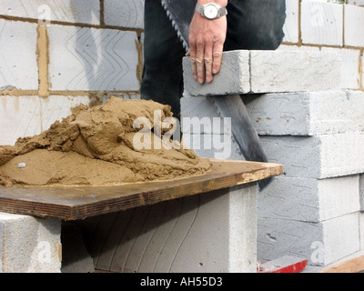 Bricklayer using hand saw to cut soft insulation blocks for cavity wall of new house with sand and cement mortar mix on mortar board England UK Stock Photo