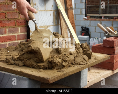Close up of bricklayers mortar board and trowel with red facing bricks and new wall Stock Photo
