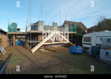 Building materials for new home under construction on infill plot of land progress on brick walls with roof trusses delivered & scaffolding erected UK Stock Photo