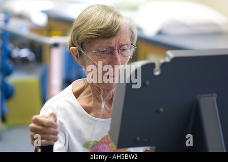 80 year old woman working out in gym on an digital exercise machine using oxygen Stock Photo
