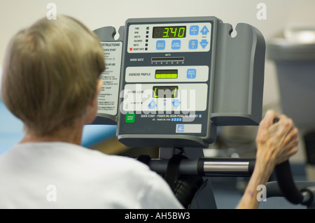 80 year old woman working out in gym on a digital exercise machine using oxygen Stock Photo