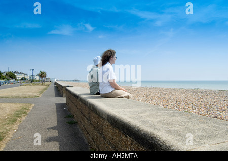 older and younger women sitting on seaside resort promenade wall looking towards the sea Stock Photo