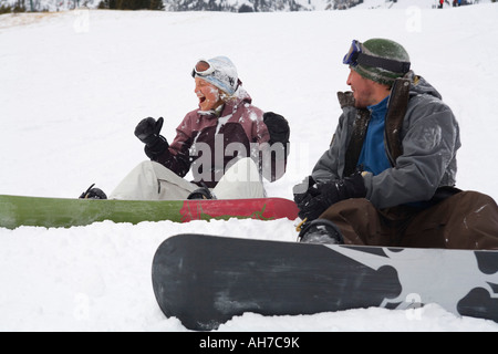 Mid adult couple sitting on snow with snowboards Stock Photo