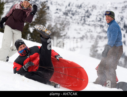 Mid adult man falling from a sled with a mid adult man and mid adult woman watching Stock Photo