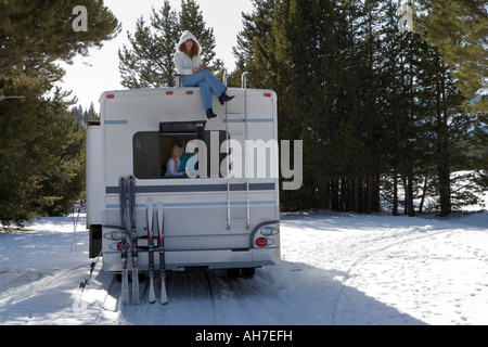 Mature woman sitting on top of a recreational vehicle with her two daughters inside it Stock Photo