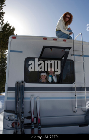 Mature woman kneeling on top of a recreational vehicle with her two daughters inside it Stock Photo