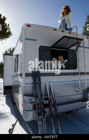 Mature woman kneeling on top of a recreational vehicle with her two daughters inside it Stock Photo