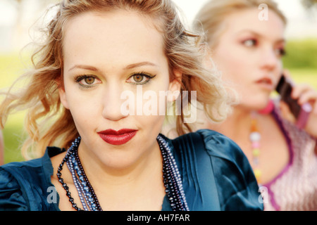 Portrait of a young woman with a young woman on a mobile phone behind her Stock Photo