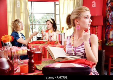 Young woman holding a book with two young women dining in a resturant behind her Stock Photo