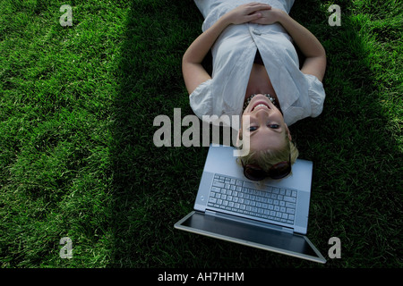 High angle view of a young woman lying in a park with a laptop under her head Stock Photo