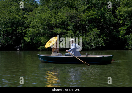 Young man rowing a boat with a young woman sitting in front of him holding a parasol Stock Photo