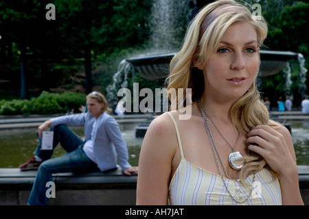 Young woman looking away with a young man sitting in the background near a fountain Stock Photo