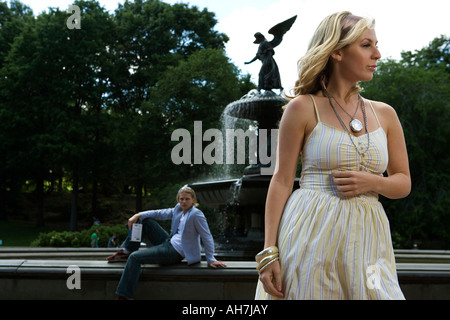Young woman standing with a young man sitting in the background, Central Park, Manhattan, New York City, New York, USA Stock Photo