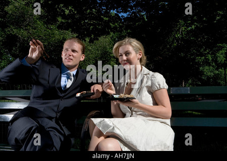 Young couple sitting on a park bench and eating sushi Stock Photo