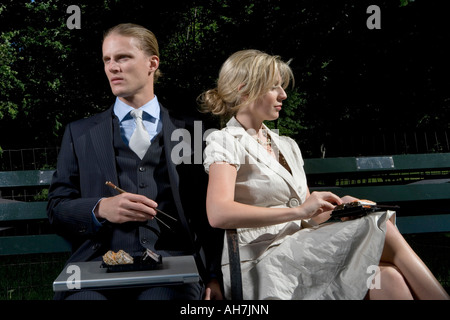 Young man sitting with a young woman on a park bench and eating sushi Stock Photo