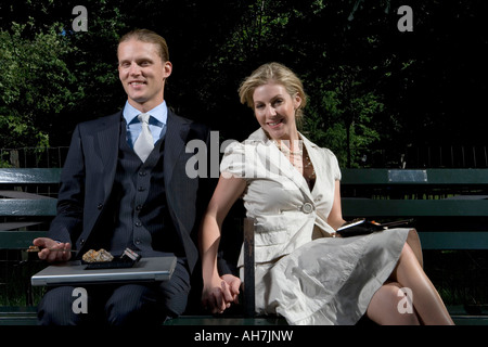 Young couple sitting on a park bench and holding hands Stock Photo