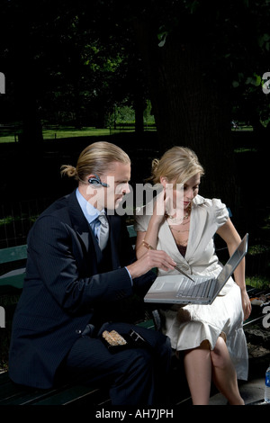 Businessman and businesswoman sitting on a park bench looking at a laptop Stock Photo