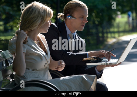 Businessman and businesswoman sitting on a park bench and looking at a laptop Stock Photo
