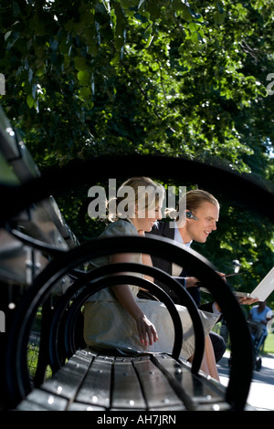 Businessman and businesswoman sitting on a park bench and looking at a laptop Stock Photo