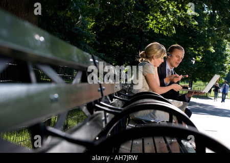 Businessman and businesswoman sitting on a park bench and looking at a laptop Stock Photo