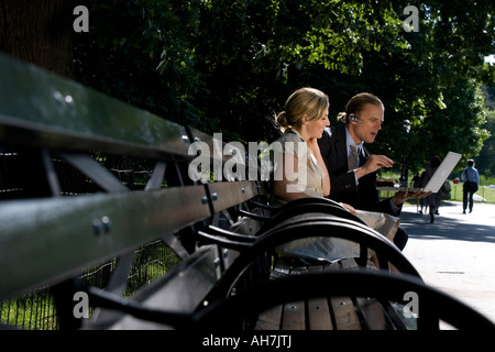 Businessman and businesswoman sitting on a park bench and looking at a laptop Stock Photo