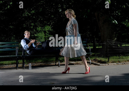 Businesswoman walking with a businessman reclining on a park bench Stock Photo