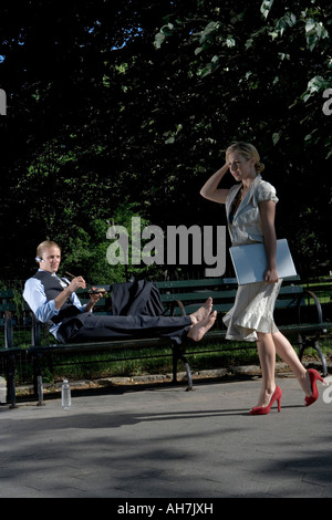 Businesswoman walking with a businessman reclining on a park bench Stock Photo