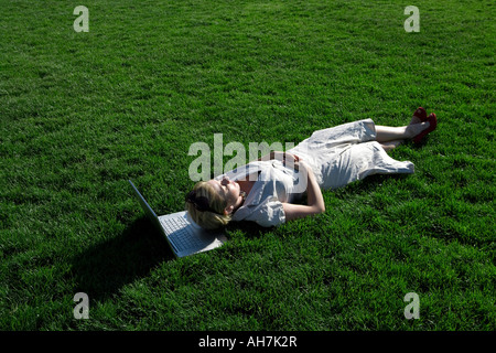 High angle view of a young woman lying in a park with a laptop under her head Stock Photo