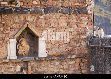 stone wall with a shrine to Mother Mary and Baby Jesus set in a niche being watched by a cat in Taormina Italy on Sicily Stock Photo