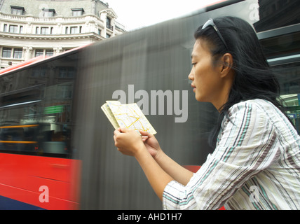 Korean oriental woman at Oxford Circus reading a map with blurred red bendy bus in background Stock Photo