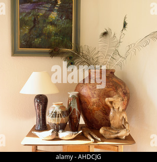 Collection of ceramic pots and seated statue on table with ceramic birds and peacock feathers in large pot Stock Photo