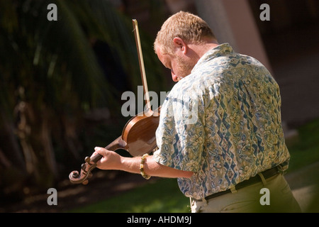 A young Caucasian street musician plays his violin in the sunshine, engrossed in his music. Stock Photo